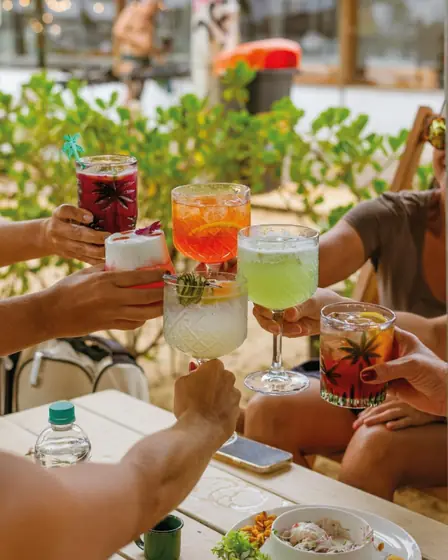 Amigos brindando com drinks coloridos na areia