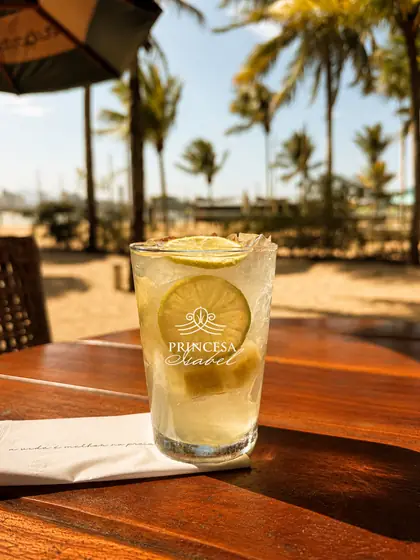 Caipirinha de limão no copo Princesa Isabel, com coqueiros ao fundo