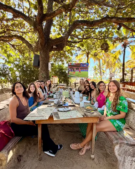 Grupo de amigas reunido em uma mesa longa na areia