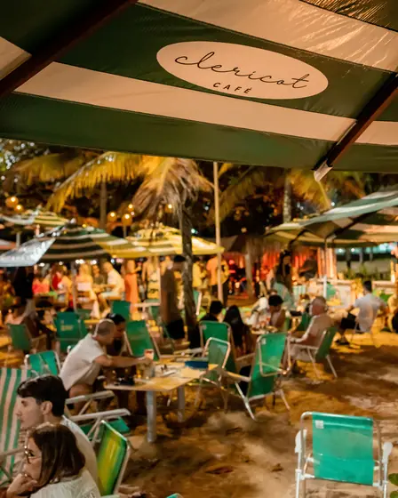Noite movimentada no Clericot, com mesas na areia sob o toldo da casa