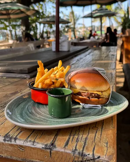 Cheeseburger com batata frita em mesa de madeira à beira da praia