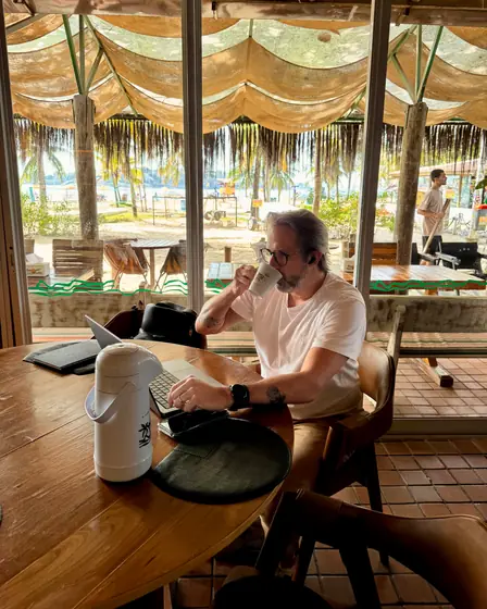 Cliente tomando café e trabalhando no notebook de frente para a praia