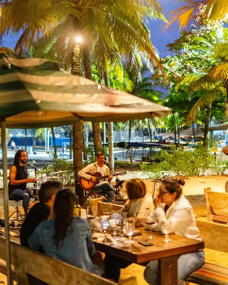 Voz e violão à noite, com mesas cheias sob os guarda-sóis