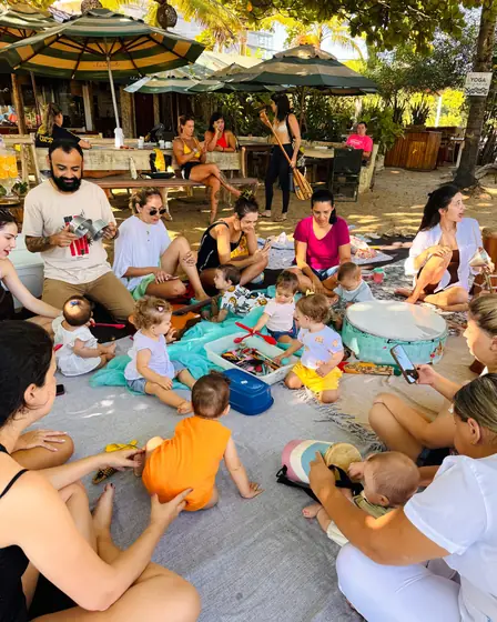 Roda de musicalização infantil com bebês e famílias na areia